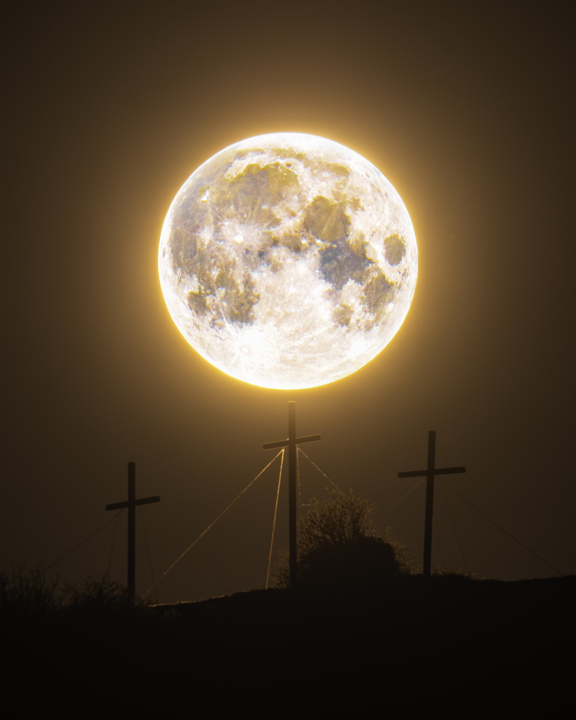An orange full moon is pictured glowing above three crosses on a hill.