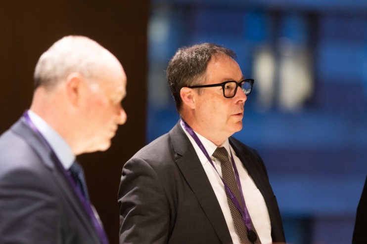 Ken Murphy delivering a keynote speech at a business conference, wearing a suit and gesturing at a presentation screen.
