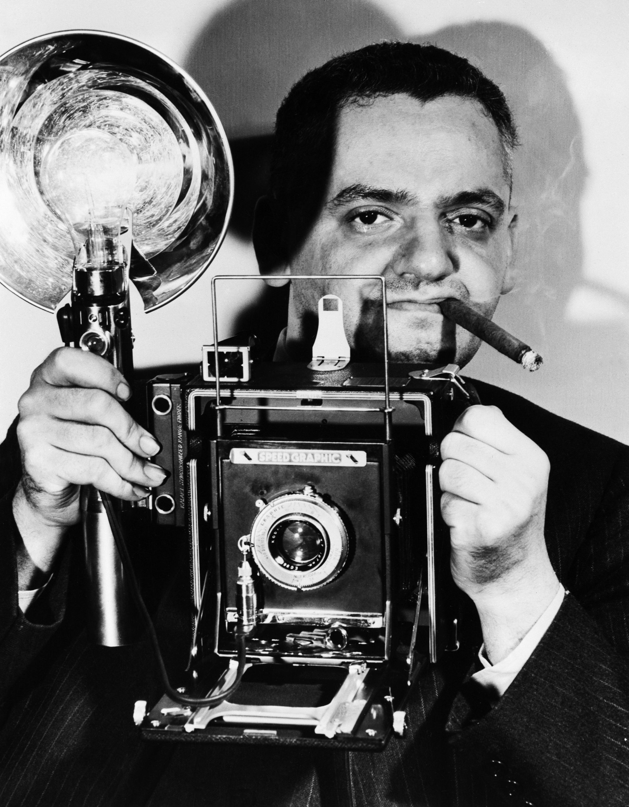 Arthur "Weegee" Fellig, holding his Speed Graphic camera and flash, with a cigar in his mouth