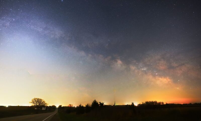 Milky Way season: Cloudy band of the Milky Way over an orange to white glow along a dark horizon.