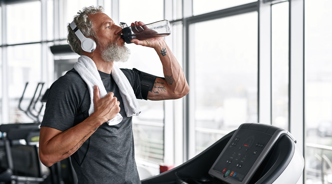 Over 50 elderly fit man drinking water after a gym workout