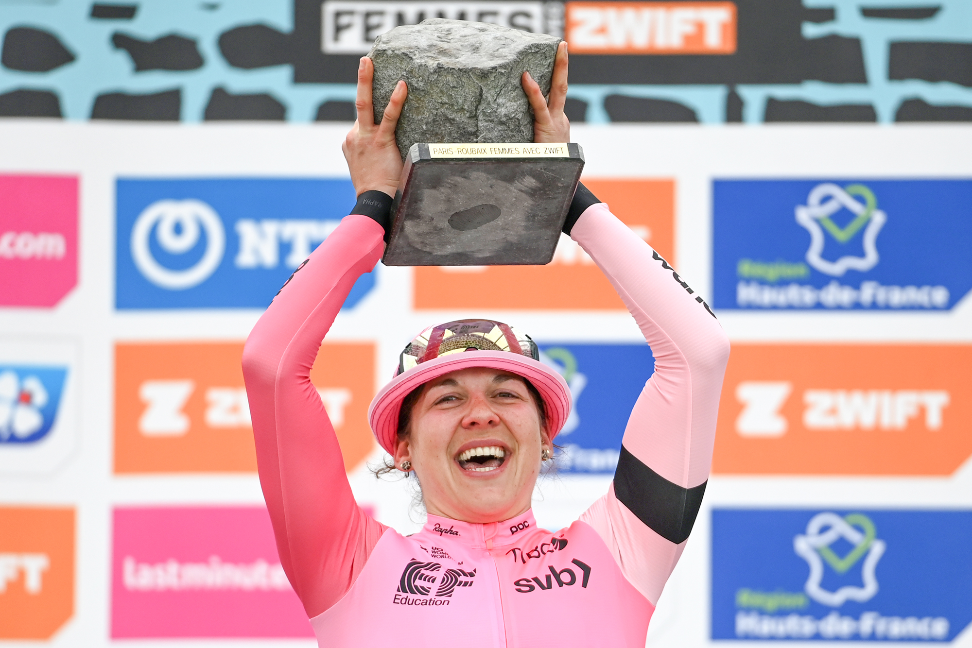 Alison Jackson celebrates with the Paris-Roubaix Femmes cobblestone trophy on the podium in 2023