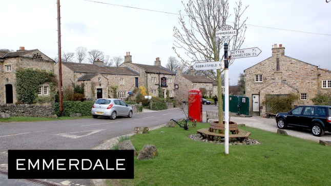A road and buildings in the Emmerdale village, with the soap logo in the bottom left hand corner.