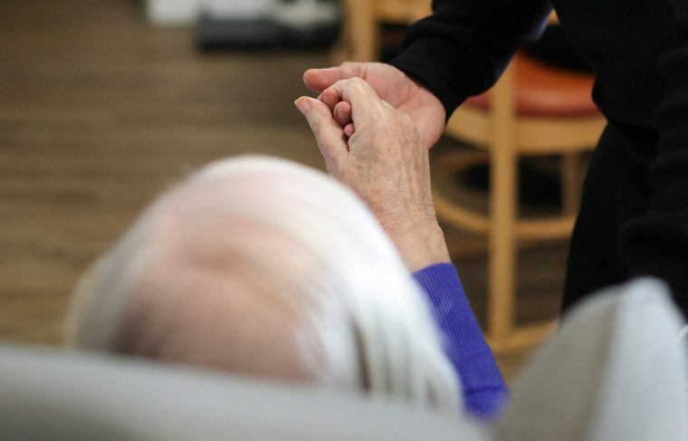 Deputy manager Kuldeep Singh holds the hand of an elderly resident at Applegarth Care Home, as the care sector braces for crisis over the British government's plans to reduce migration numbers, in Maidenhead, Britain, March 11, 2026. REUTERS/Isabel Infantes