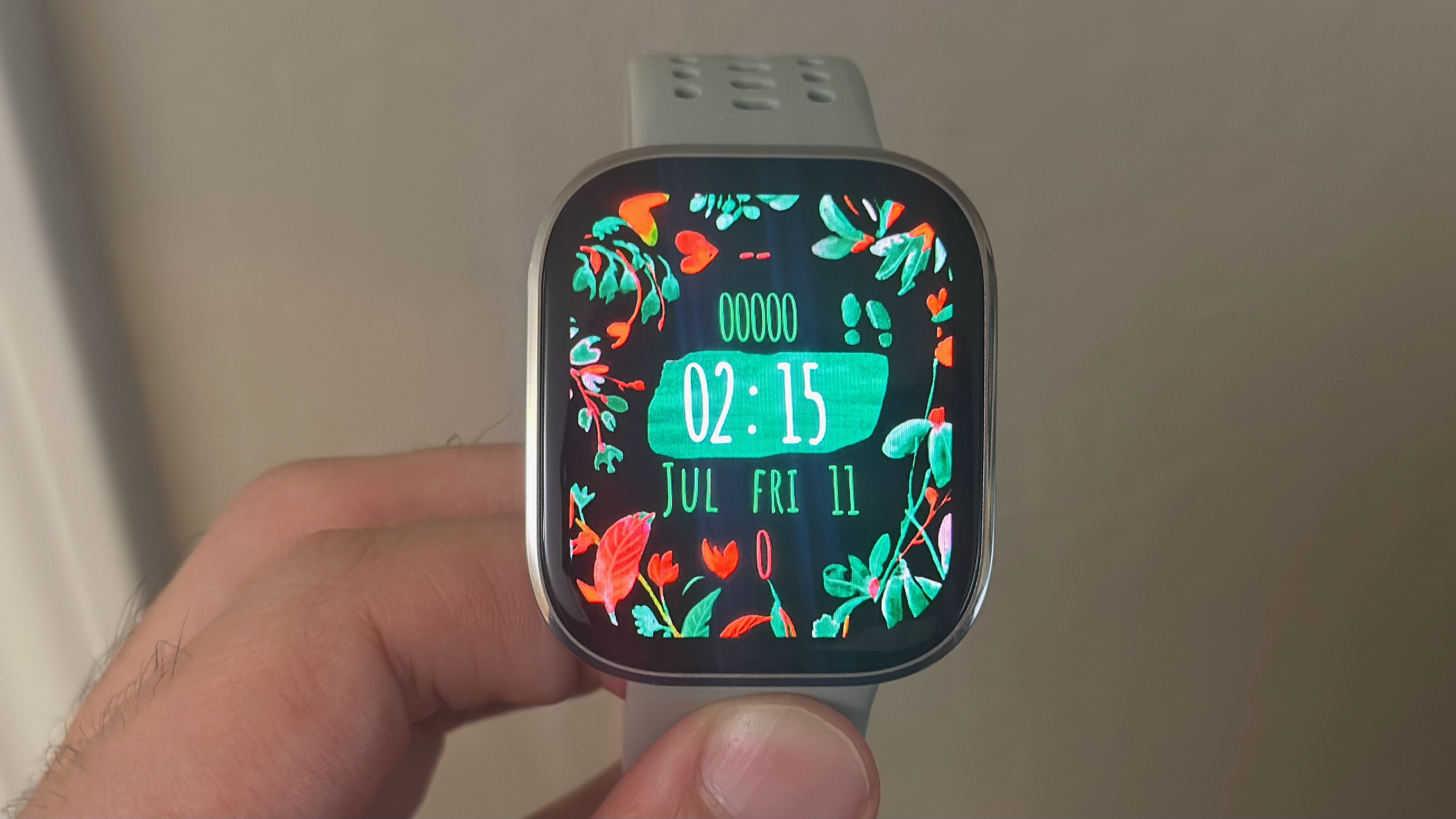 A photo close-up of the Amazfit Bip 6 held in hand, showing a custom watch face with flowers and artsy text.