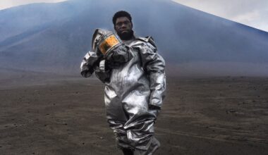 Phillip, a self-taught volcanologist, stands barefoot atop a volcanic rock bomb. Wearing a lava-protection suit, the volcano smoulders behind him, sending a plume of gas and sulphur into the sky