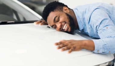 Happy African American Man Hugging New Car In Auto Dealership