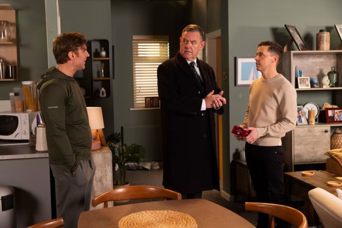 coronation-street-early-release George looks at Theo with an alarmed expression who stands with his hands in pockets. Todd stands holding a box of tea bags.