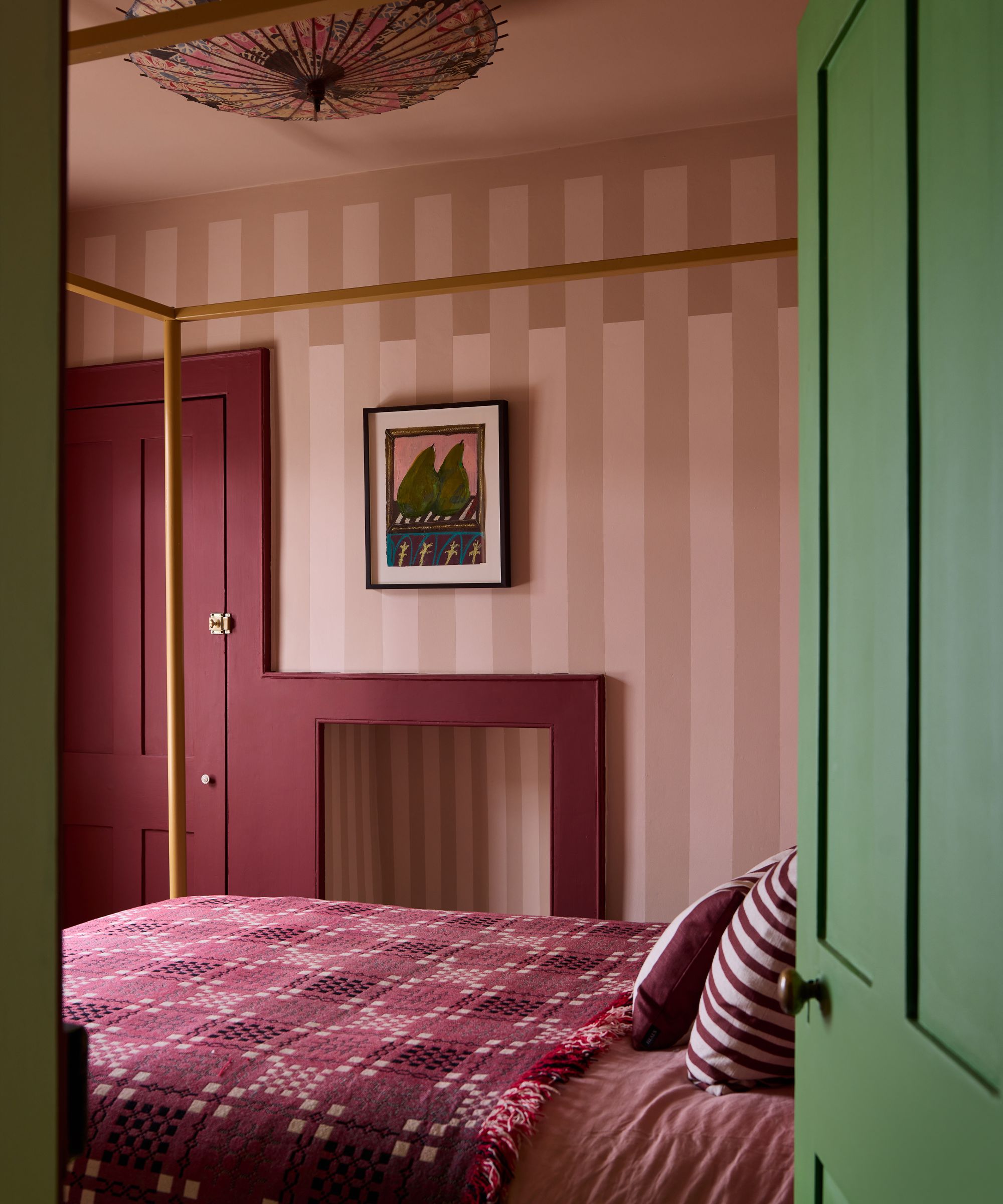 A bedroom with thick pink striped wallpaper, red and pink bedding, a dark red door and woodwork, and a dark green paint used on the door leading into the room.