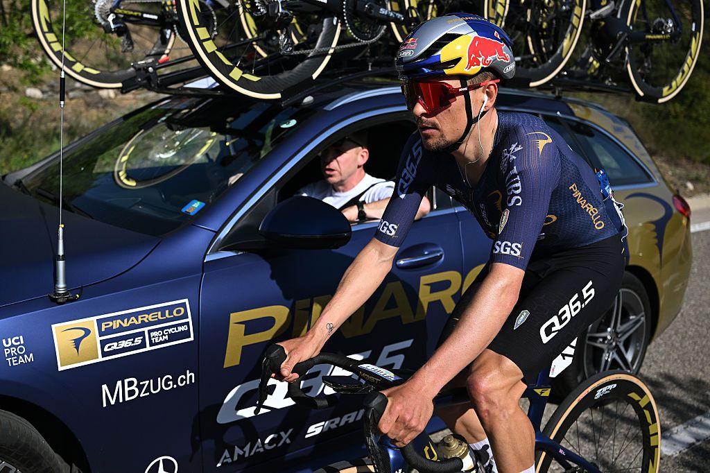 Side shot of Tom Pidcock riding next to his Pinarello-Q35.5 team car during a stage of the Volta a Catalunya