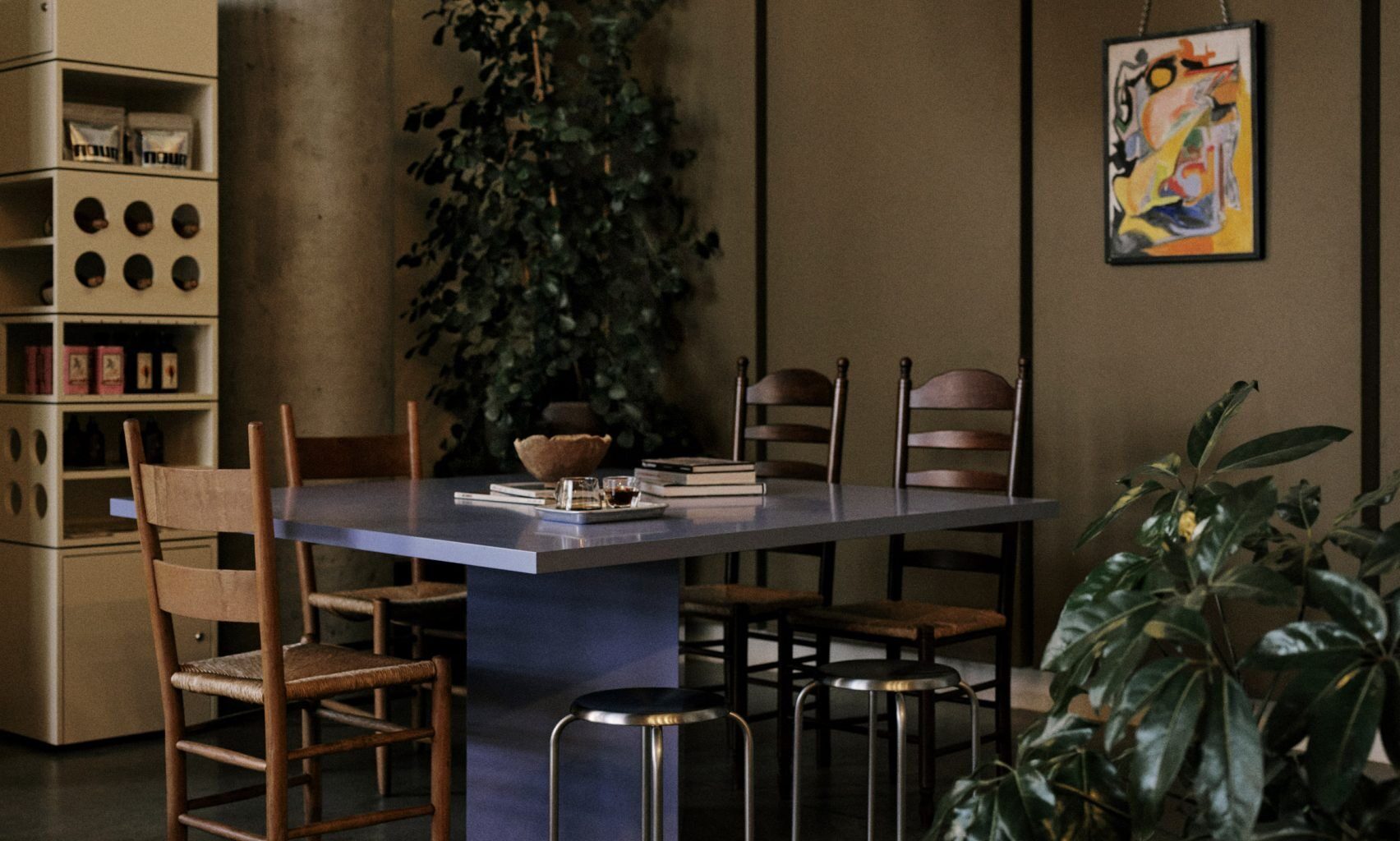 A home-looking coffee shop decorated with modernist furniture including spherical paper lanterns as lights, wood and chrome minimalist furniture, chrome table lamps, and thriving plants.