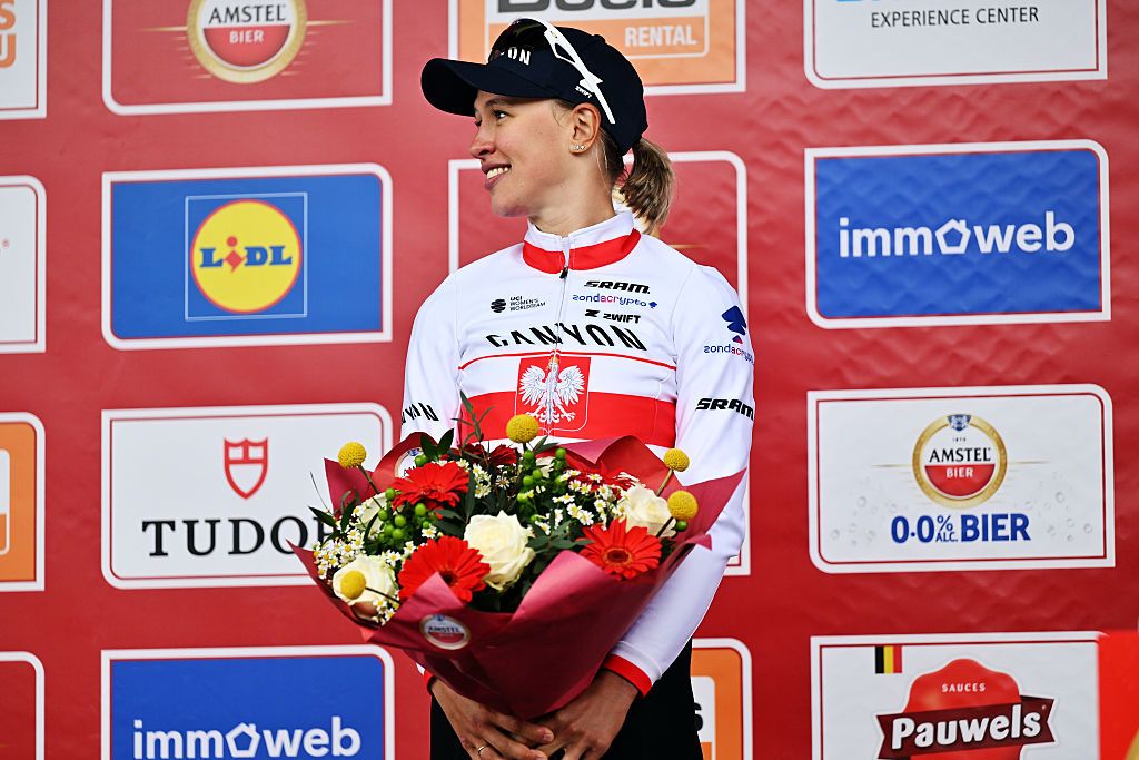 Kasia Niewiadoma-Phinney stands on the podium of Amstel Gold Race 2026, smiling to the side and holding a bunch of flowers in front of her