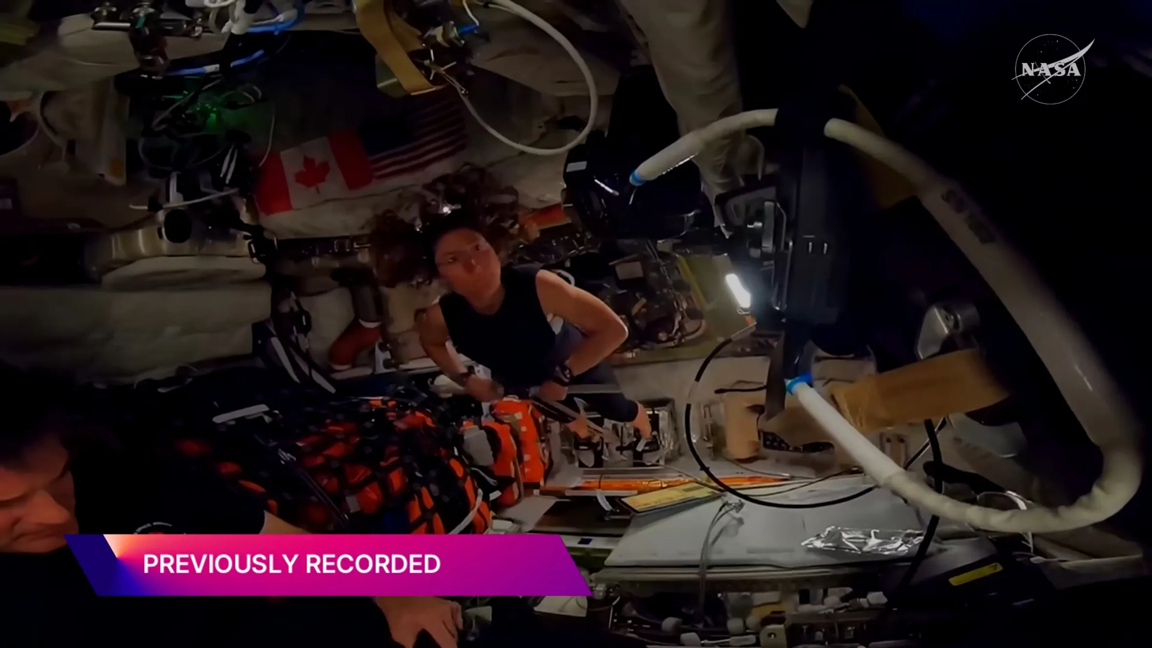 An astronaut using an exercise machine in a spacecraft, with American and Canadian flags in the background.
