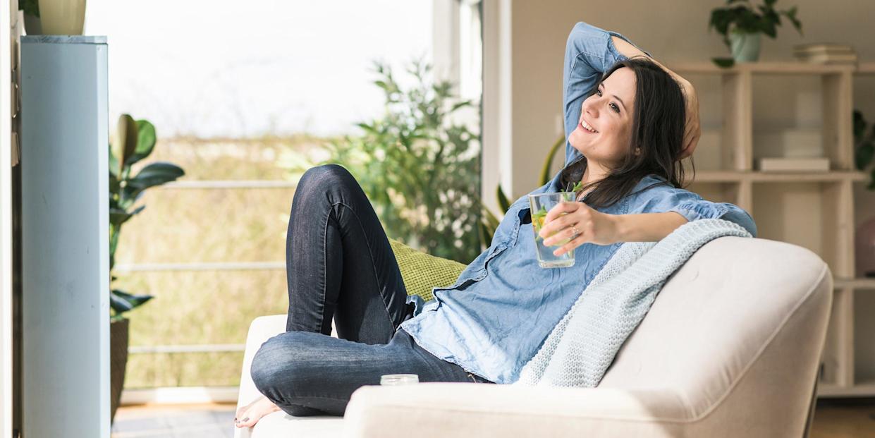 Happy woman with a glass of infused water sitting on the couch at home