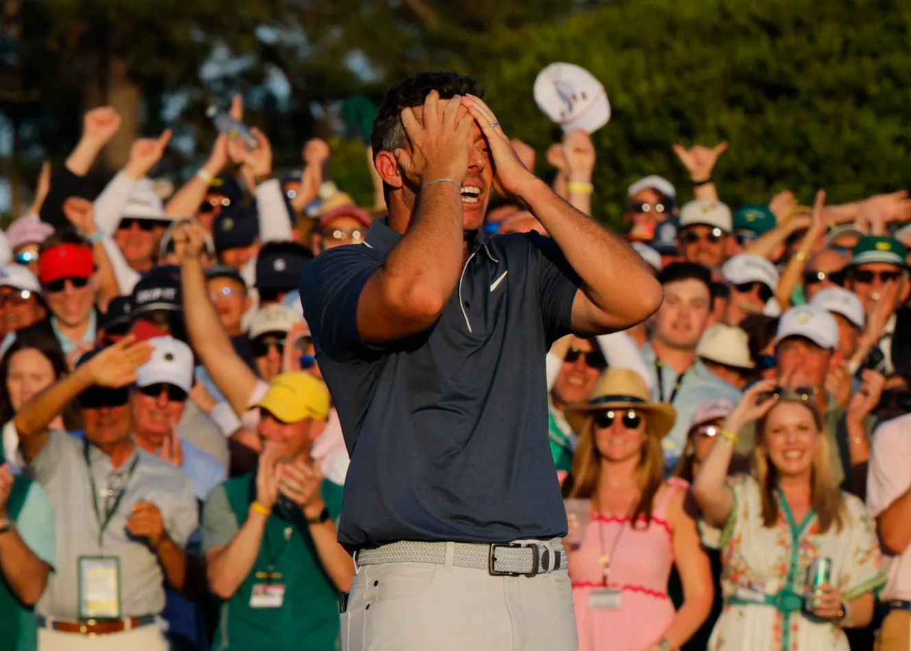 Rory McIlroy celebrates his Masters victory and career Grand Slam with hands on his head in front of a cheering crowd.