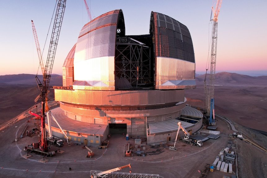 Dome-shaped building surrounded by cranes on a desert mountaintop.