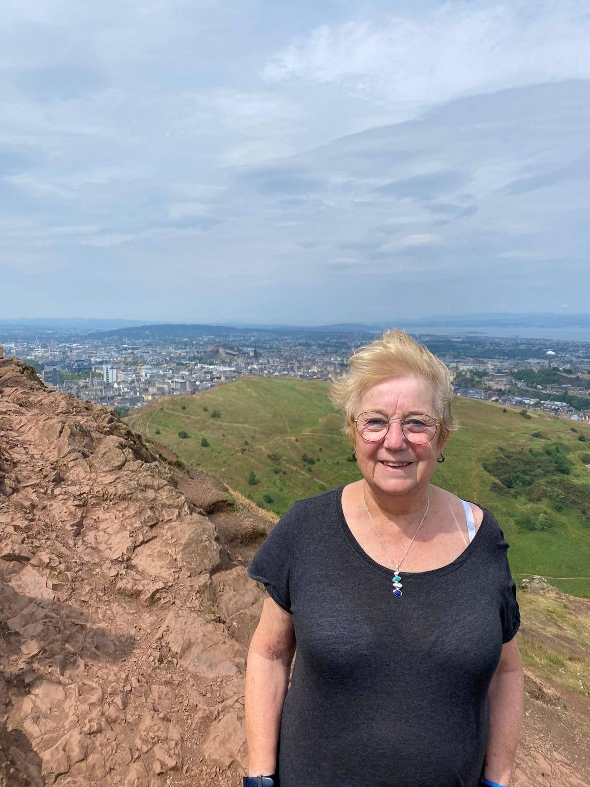 woman very windswept at the top of Arthur's Seat
