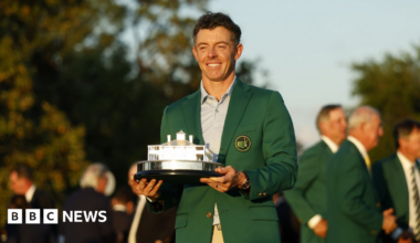 Rory McIlroy, a man wearing a green jacket and holding a silver trophy for winning the Masters in Augusta.