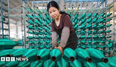 A woman stacks rolls of bright green fishing nets on a production line at factory