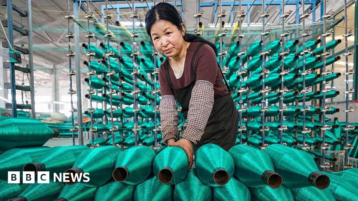 A woman stacks rolls of bright green fishing nets on a production line at factory
