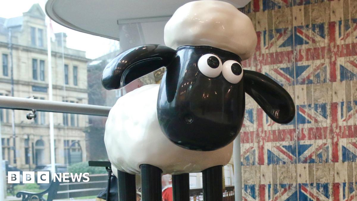 The original black and white Shaun the Sheep animation has been created into a sculpture. It has been positioned on a platform in front of a large glass window and a wall featuring Union Jack flag wallpaper.