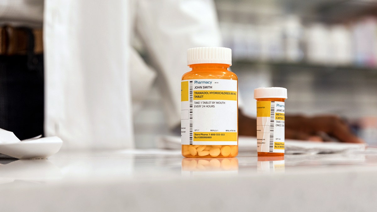 A person in a lab coat stands behind two prescription pill bottles.