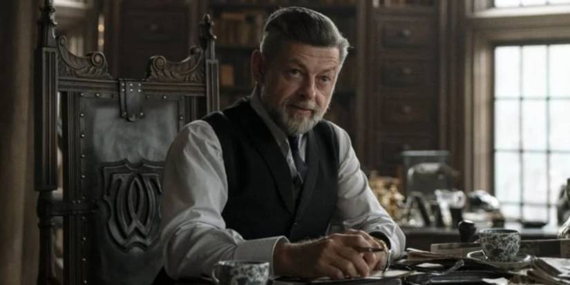 Andy Serkis as Alfred sitting at a table in a library or study room inside Wayne Manor in The Batman.