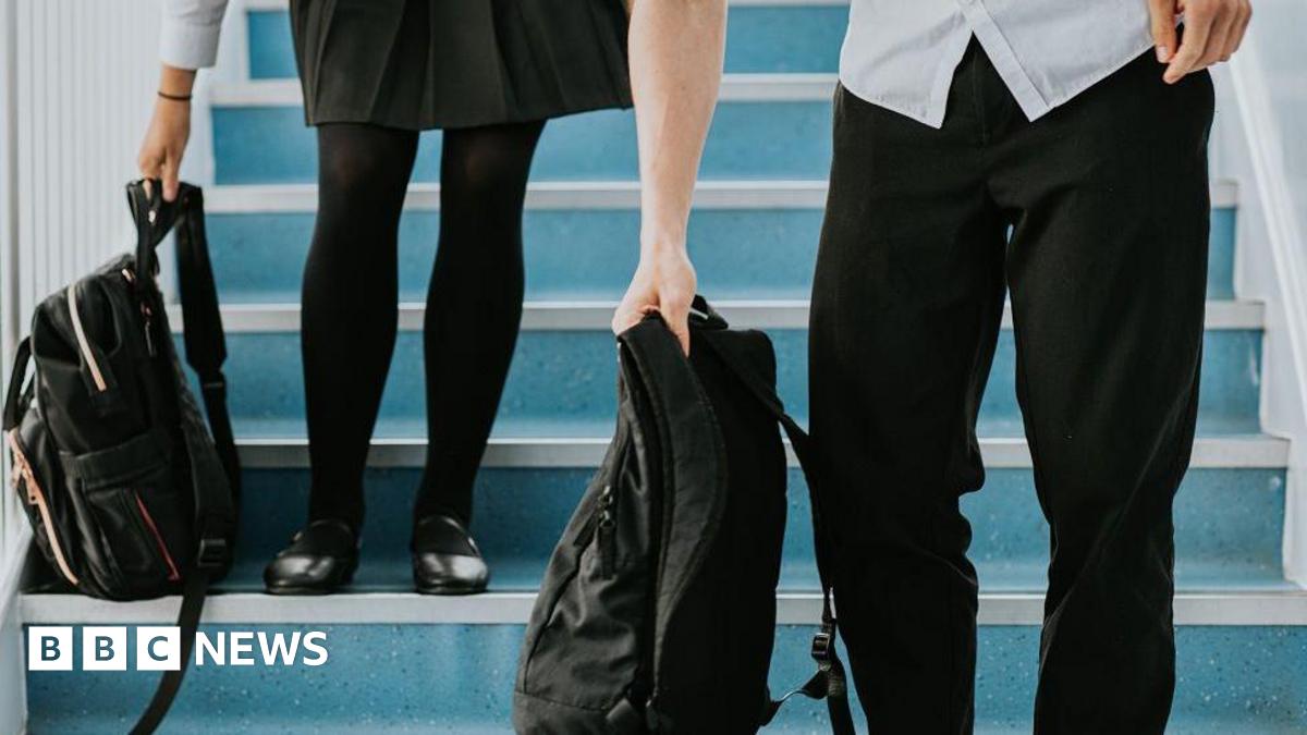 A boy and a girl senior high students stand up from the steps they were sitting on as the bell rings. They grab their school bags to take to the next class. Only their uniforms (skirt and trousers) and below are visible.