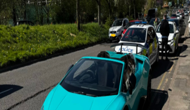 A teal-coloured Lamborghini on the side of a road with two police vehicles in the background