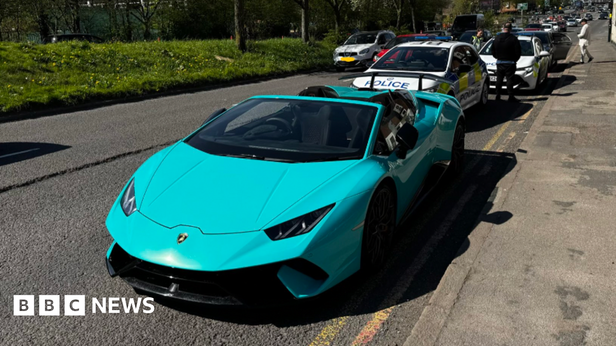 A teal-coloured Lamborghini on the side of a road with two police vehicles in the background