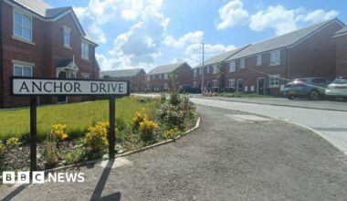 A sign reads Anchor Drive as the road leads round into a residential area - with houses on both sides of the road and cars in the drive