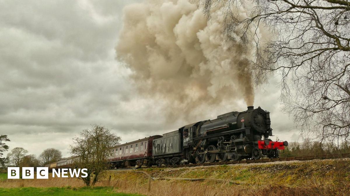 An old train on the Churnet Valley Railway emits steam as it travels along the track through the countryside.