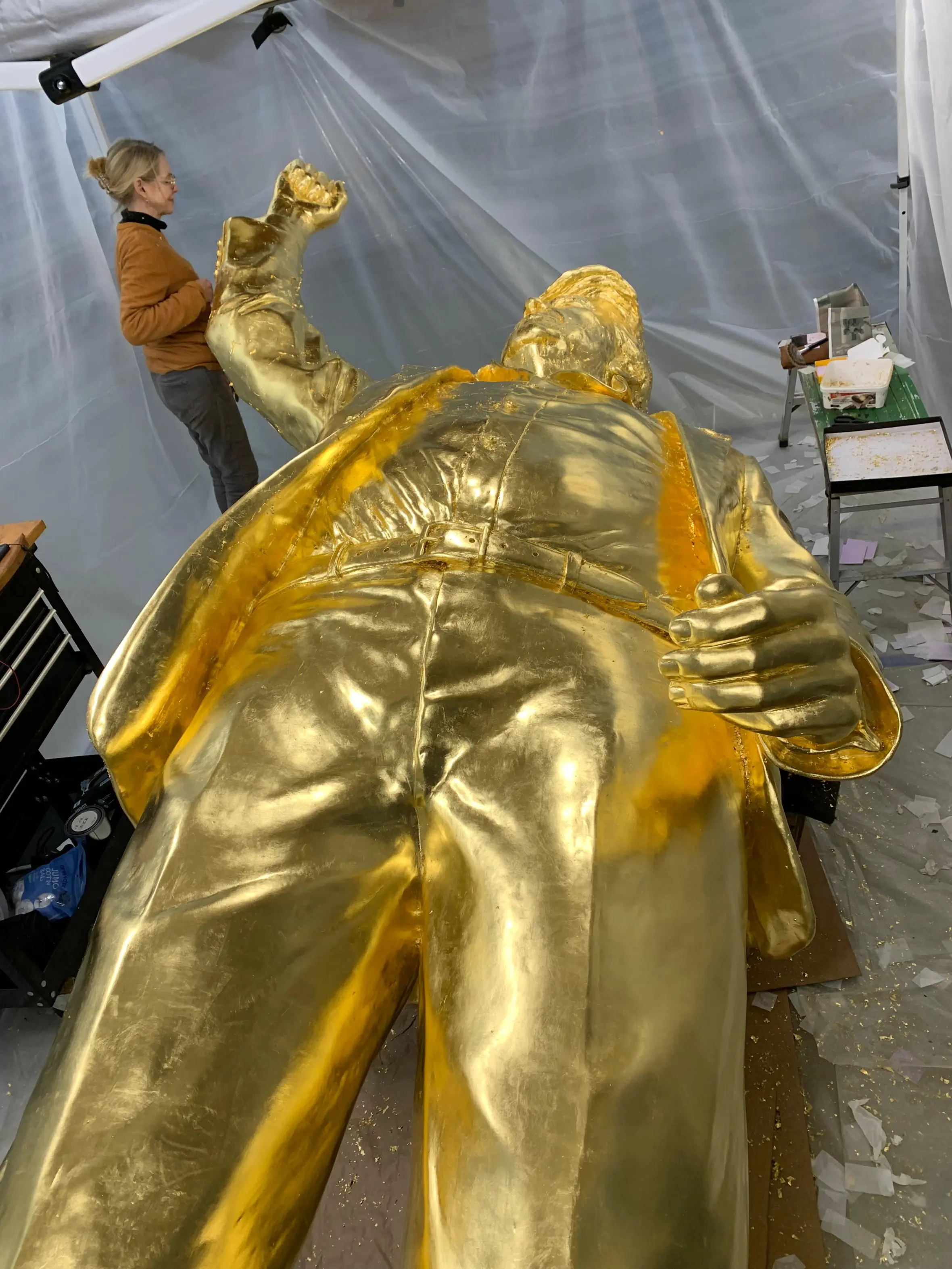 A woman working on a giant golden statue of a man.