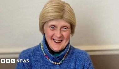 Woman with short blonde hair smiling at camera in blue wool cardigan and beaded necklace