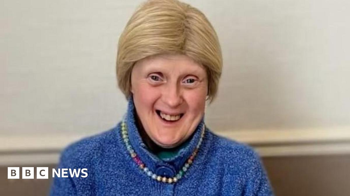 Woman with short blonde hair smiling at camera in blue wool cardigan and beaded necklace