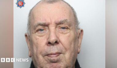 A mugshot of a elderly, balding man with grey hair.