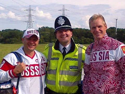 Mark Bullen, a former British police officer, smiling between two men wearing "Russia" apparel.