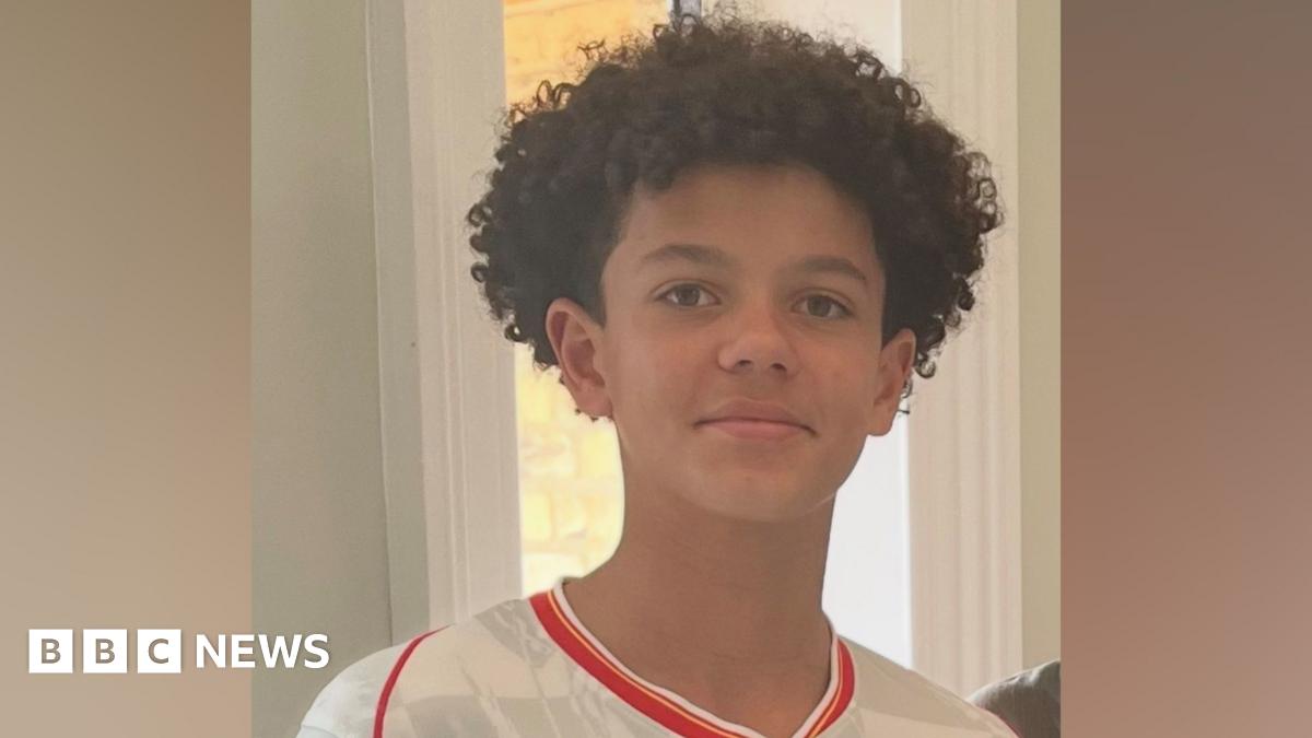 Noah smiling at the camera. He is wearing a white football shirt with red edging and has short curly hair.