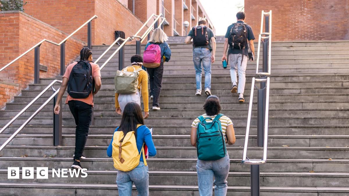 A diverse group of students, dressed in jeans, with many different coloured rucksacks on their backs are climbing steps outside on university campus.