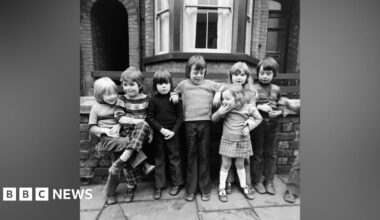 Black and white photograph of seven young children aged three to seven, in typical 1970s clothing, stood on a residential street with a Victorian house behind