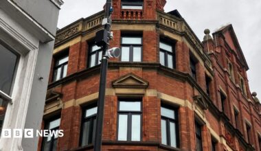Image shows Laura Macmillan, a classically trained musician. She is holding a violin in each hand. Laura is wearing a black dress and has long blonde hair.