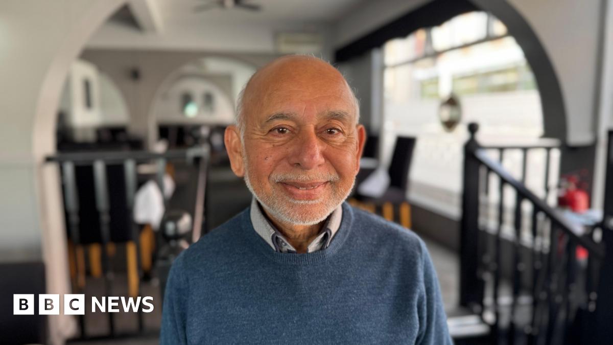 Nathan sitting in a pub with a drink. He is wearing a blue tracksuit top and has his arms crossed. He has a short beard and dark brown hair.