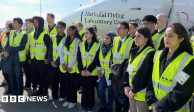 Students from Luton wearing high-vis jackets pose for a photo in front of an aircraft - the National Flying Laboratory Centre.