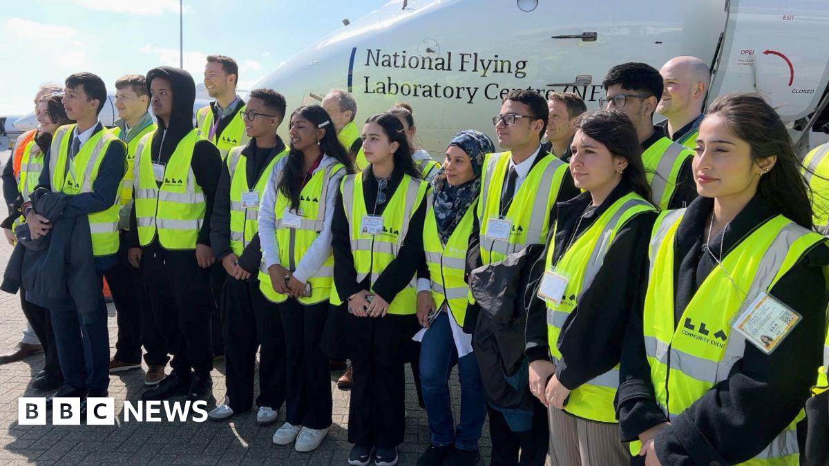Students from Luton wearing high-vis jackets pose for a photo in front of an aircraft - the National Flying Laboratory Centre.