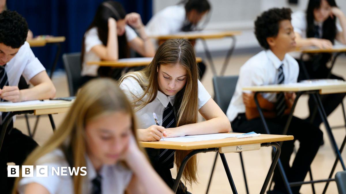 Teenage girl wearing school shirt and tie writing in exam booklet, arm resting on desk