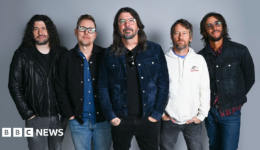 Five members of the Foo Fighters band stand side by side looking directly at the camera, hands in pockets.