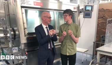 A scientist gives a demonstration about space rocks in a room filled with shiny space tech