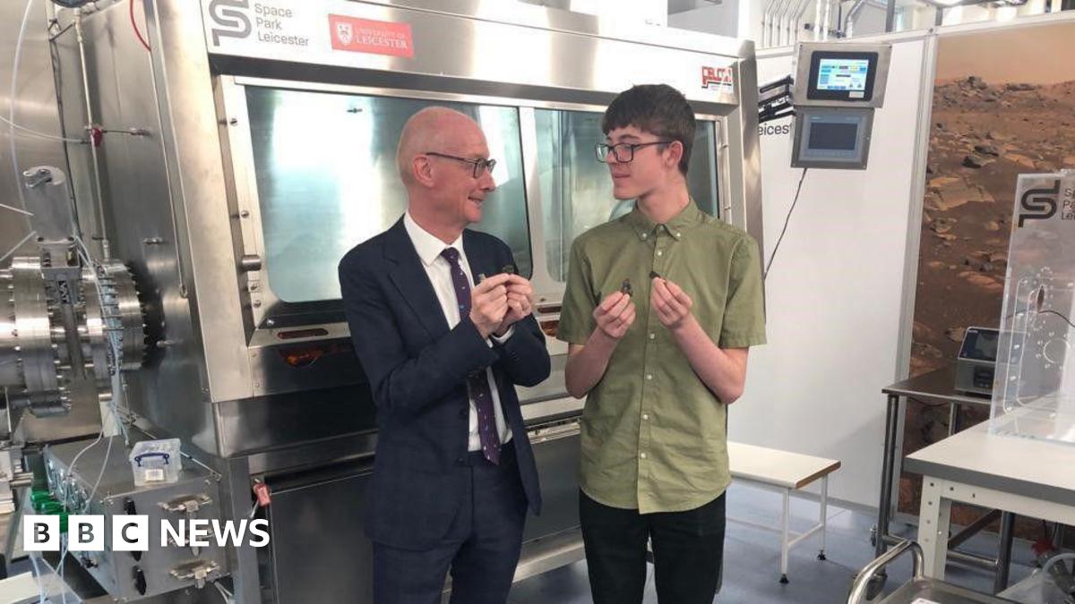A scientist gives a demonstration about space rocks in a room filled with shiny space tech