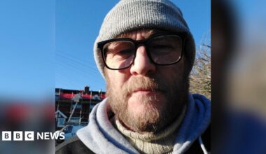 Scott Brooks, a man in his late 40s with a brown-haired beard and glasses, wearing a beanie hat.
