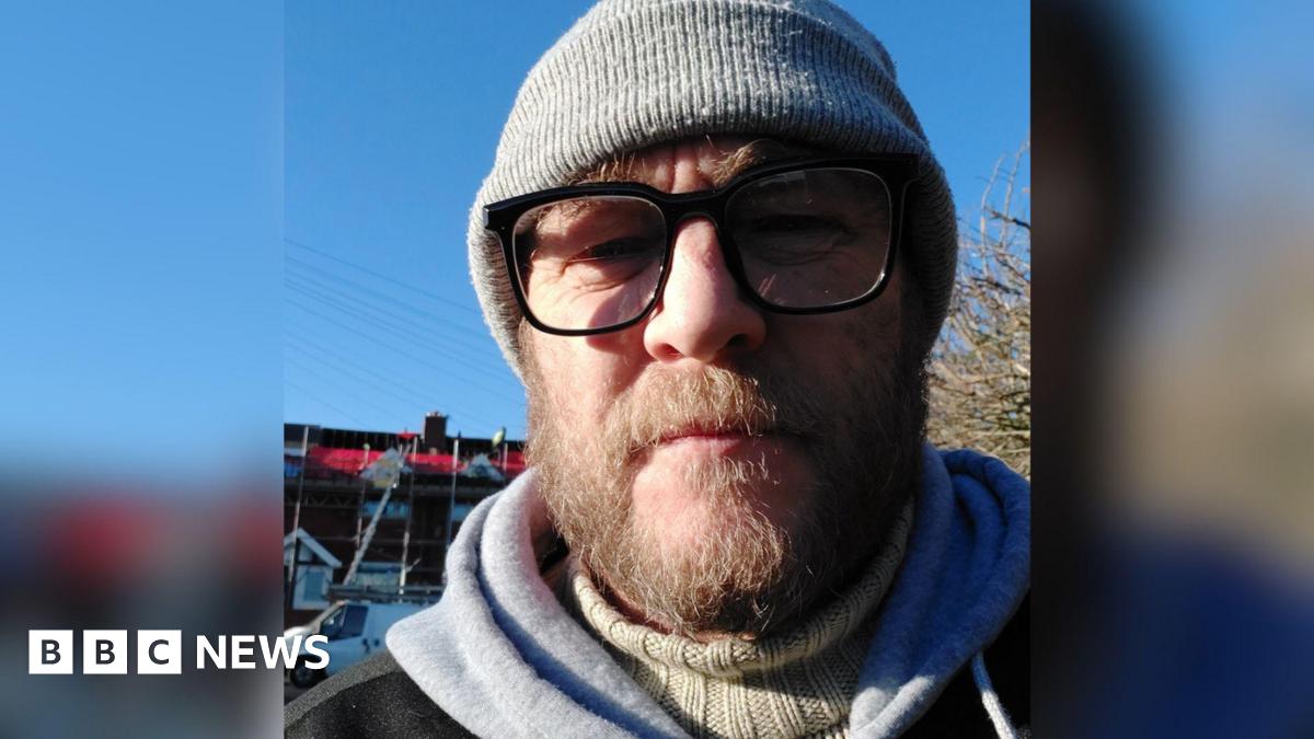 Scott Brooks, a man in his late 40s with a brown-haired beard and glasses, wearing a beanie hat.